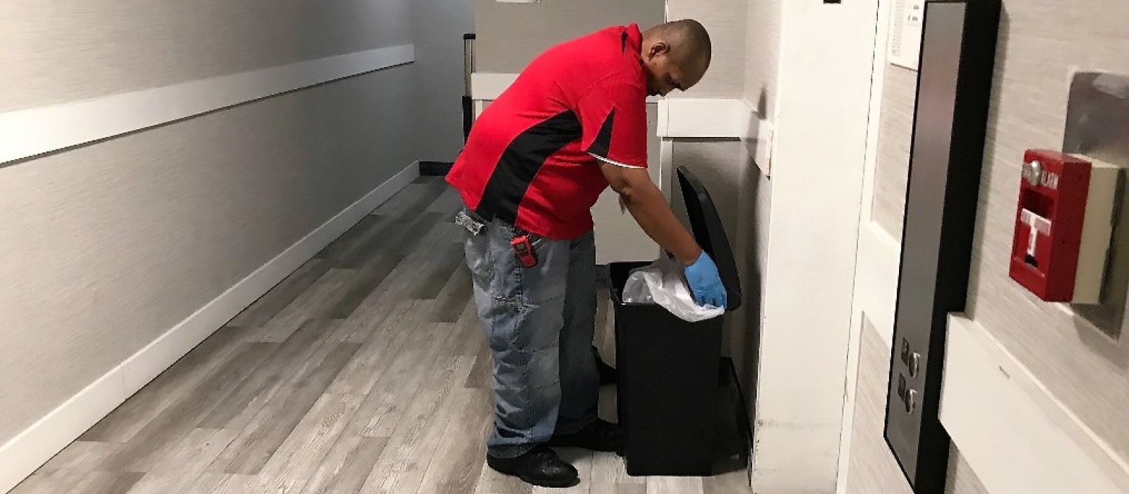 LCS participant wearing a red shirt and gray pants is changing a trash bag in a trash can